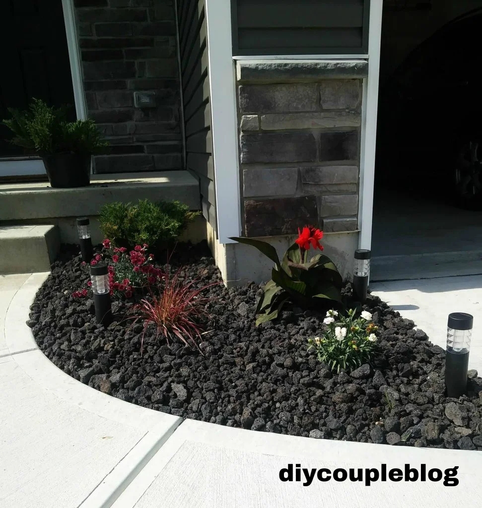 black lava rock landscaping in a small flower bed by garage