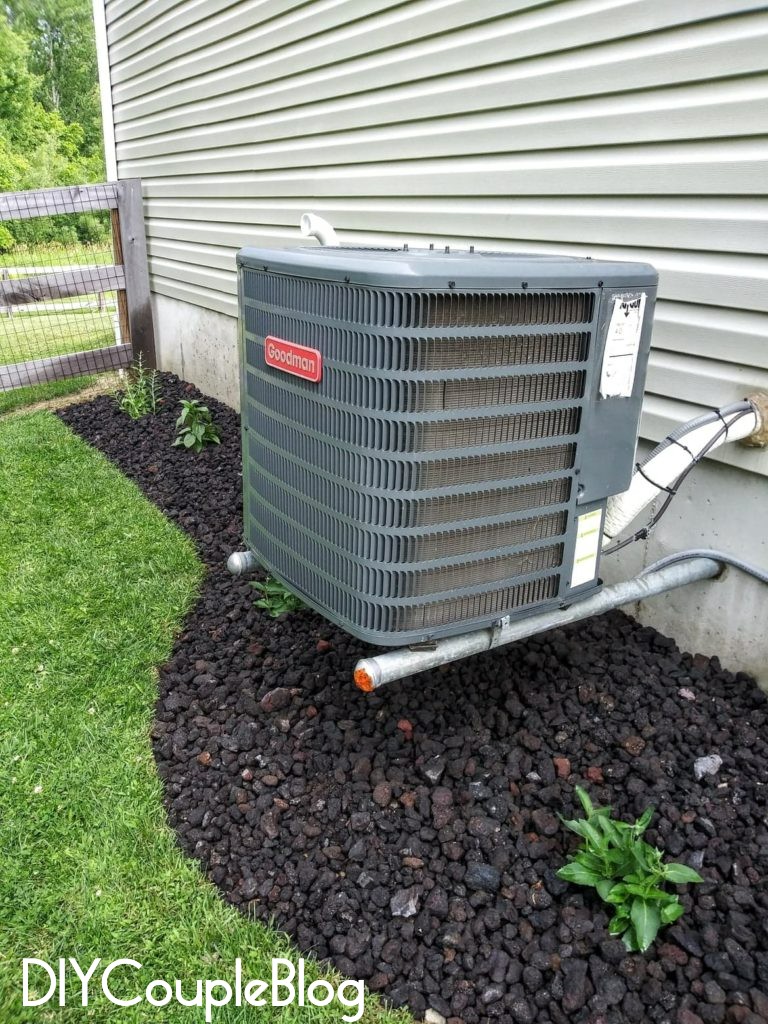 black lava rocks around ac unit on the side of the house