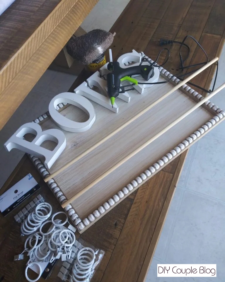 craft supplies including a wooden sign, dowel rods, curtain clips, hot glue gun and staining supplies laid out