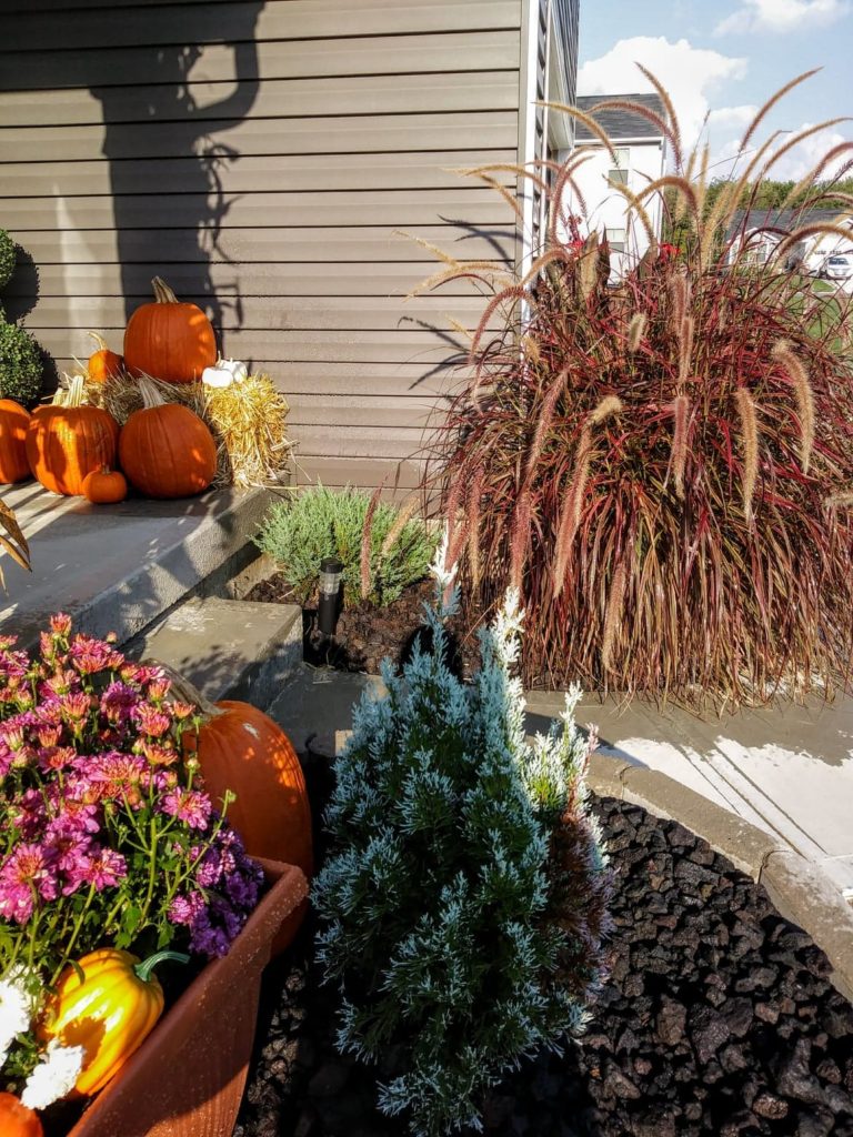 decorating with pumpkins, fall plants, and bale of hay on porch