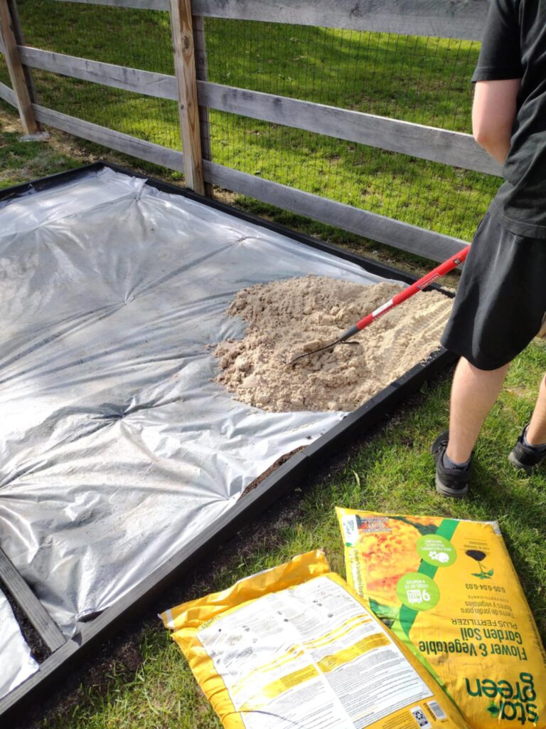 spreading sand with metal rake inside DIY sandbox