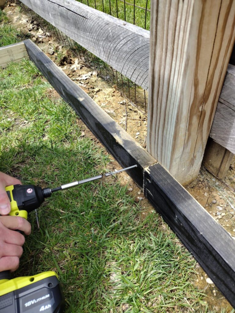 attaching the DIY sandbox side of the playground border to the fence