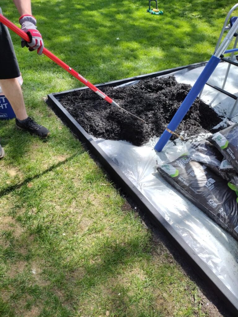spreading mulch with a metal rake around our swing set and playground border
