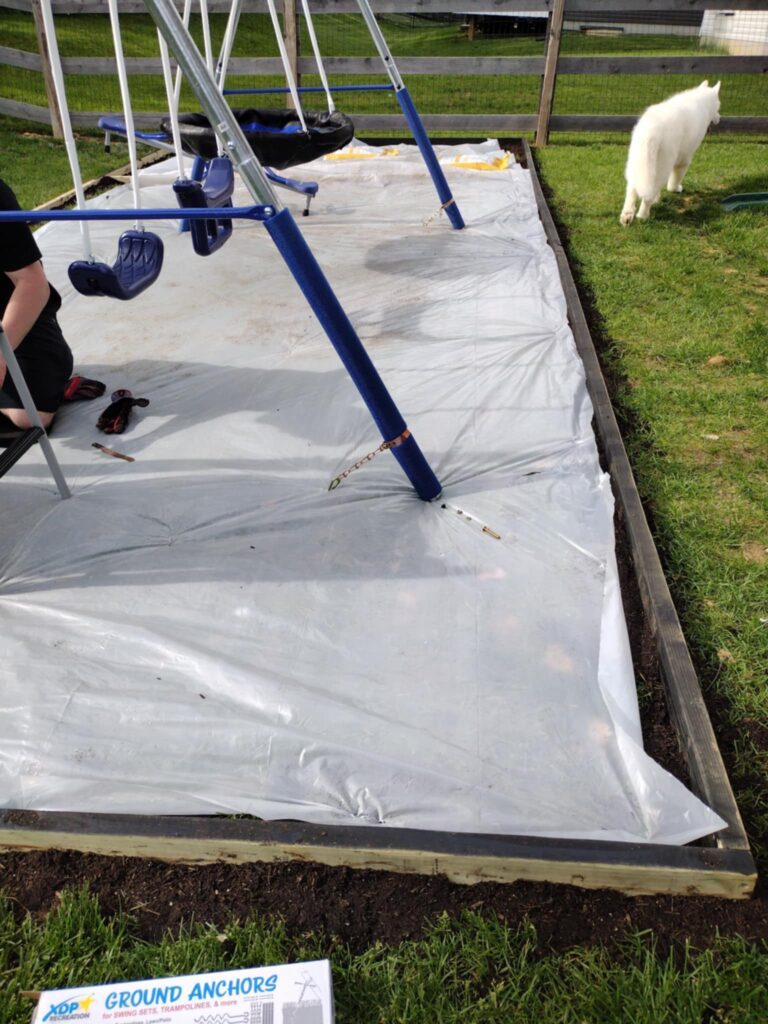 laying plastic sheet over the grass for the backyard playground