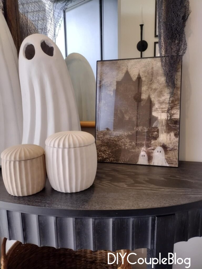 halloween decorations on a black console table with ghosts and printable wall art in a frame