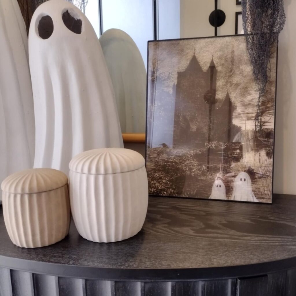 halloween decorations on a black console table with ghosts and printable wall art in a frame