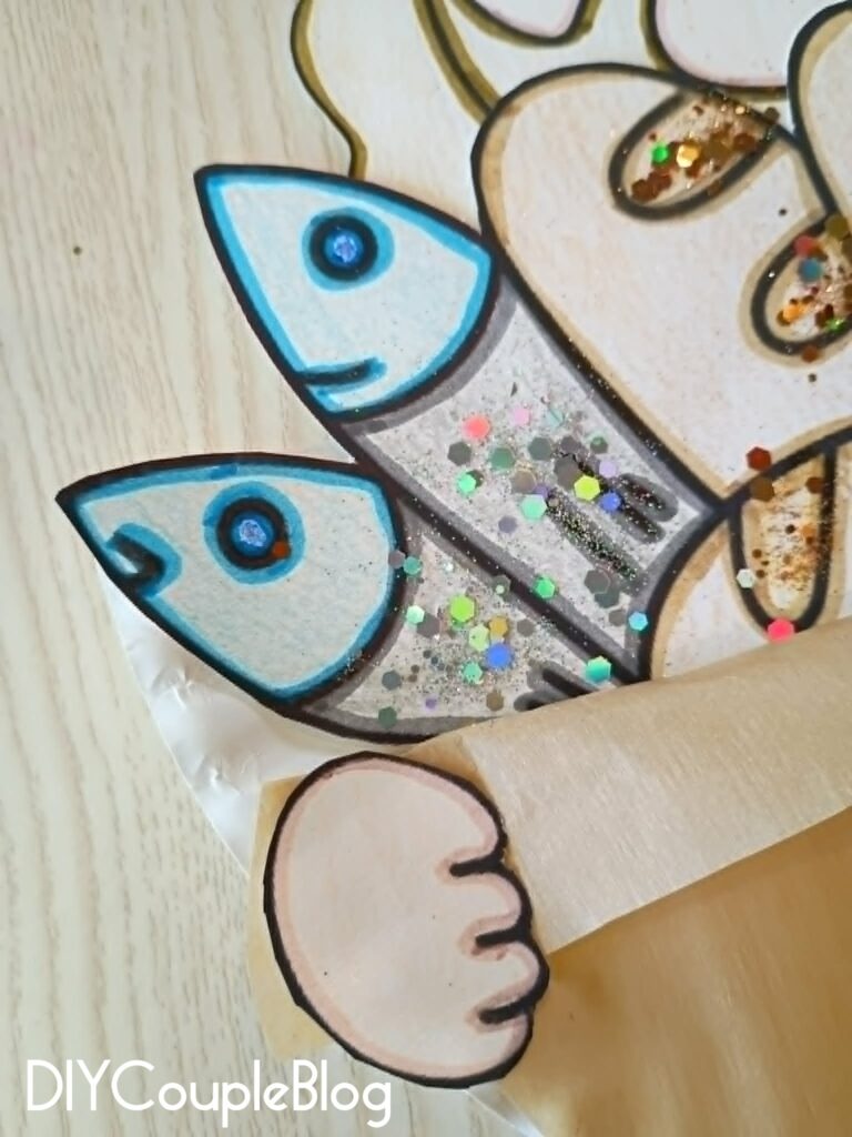 adding glitter to my finished fish craft for Jesus feeds 5000