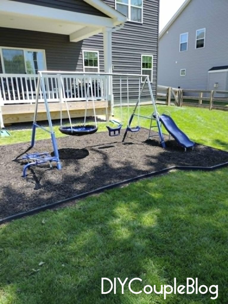 blue metal swing set with black mulch and black DIY border around it