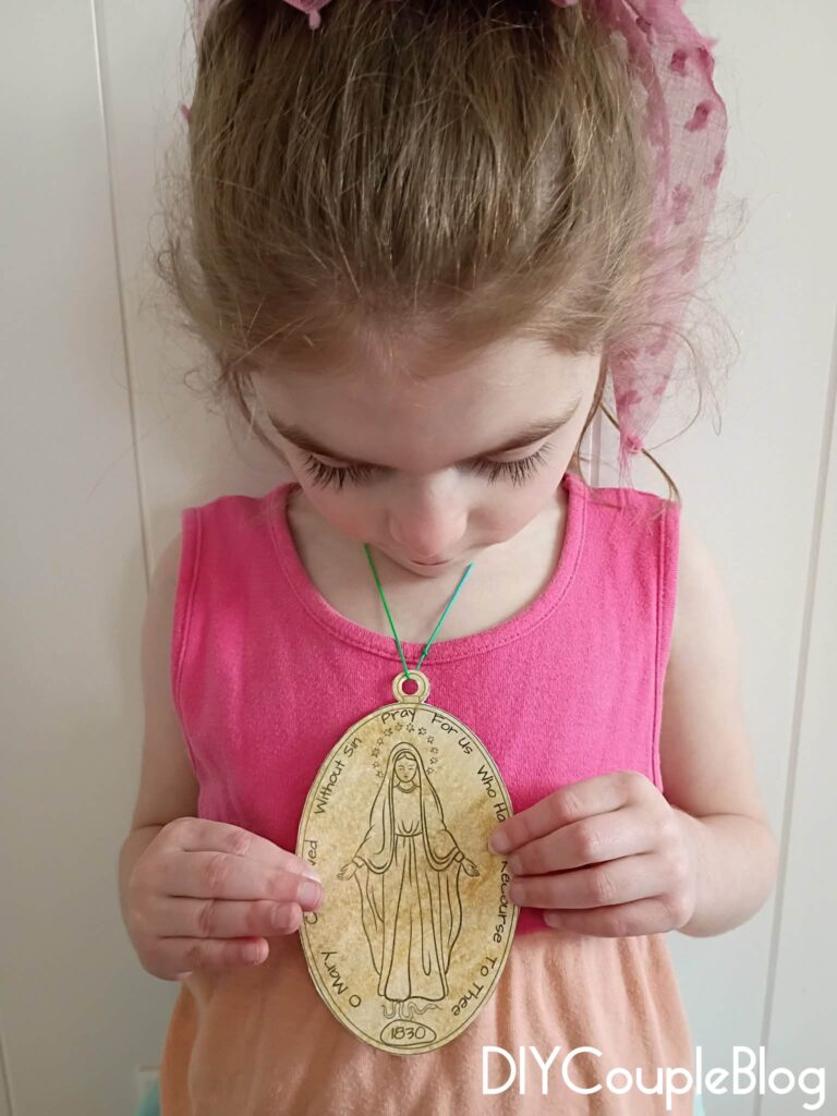 girl holding and showing the front of catholic printable miraculous medal craft necklace