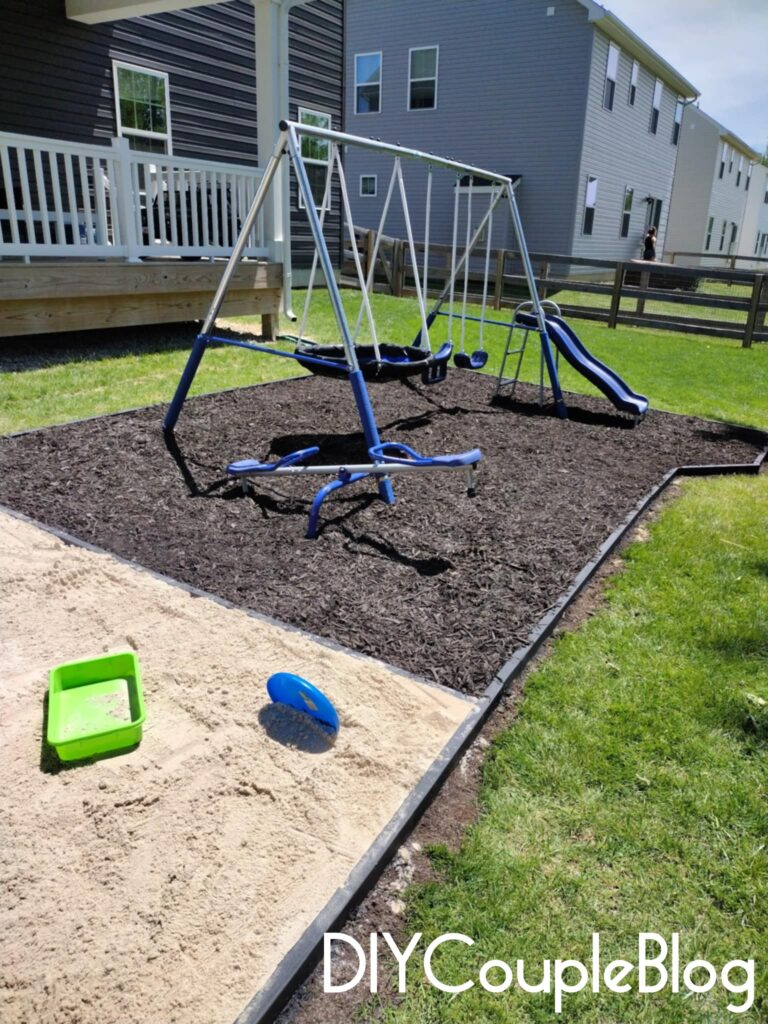 side angle of our small backyard playground with black 2x4 wood boards and black mulch