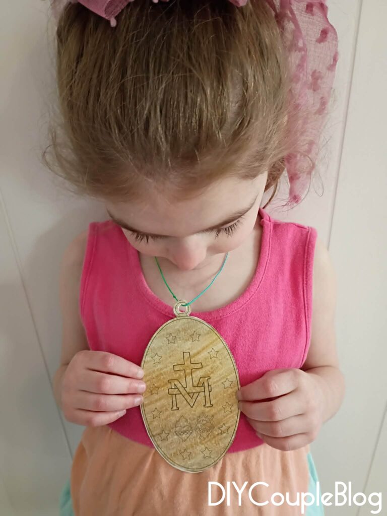 girl holding and showing the back of catholic printable miraculous medal craft necklace