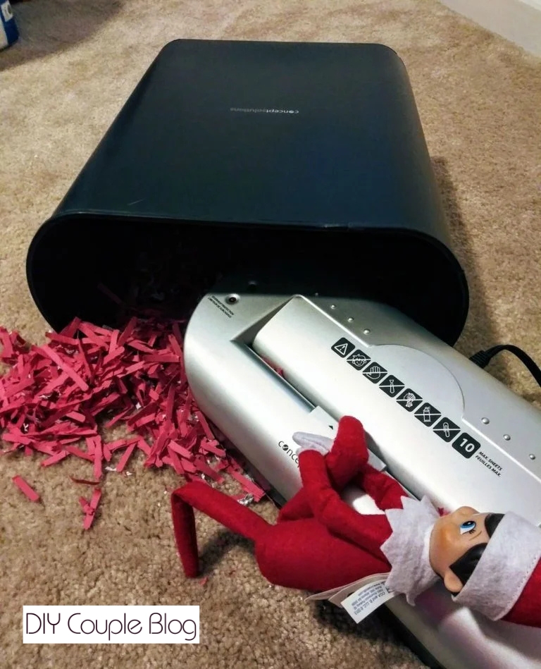 elf getting a leg caught in the shredder with shredded red construction paper 